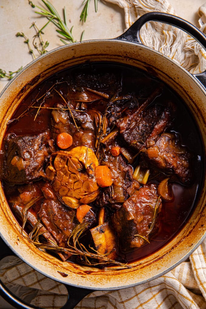succulent red wine braised short ribs in large black pot with fresh herbs on the side